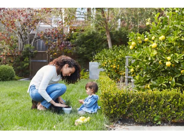 a mom and her baby in the backyard planting something in a pot
