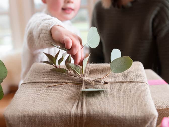 Image of child putting leaves in twine bow wrapped around muslin wrapped box