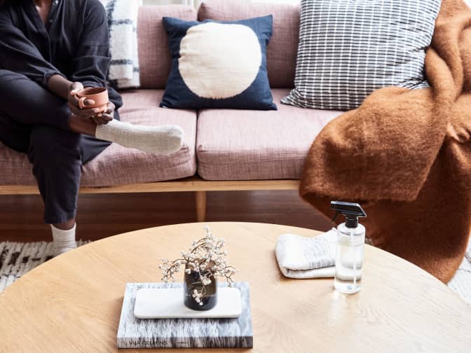 Photo of person sitting on couch near coffee table with spray bottle on it