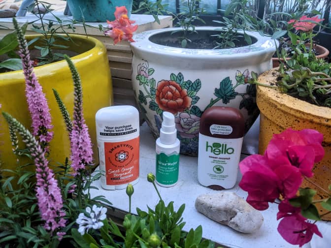 Photo of three natural deodorants surrounded by plants