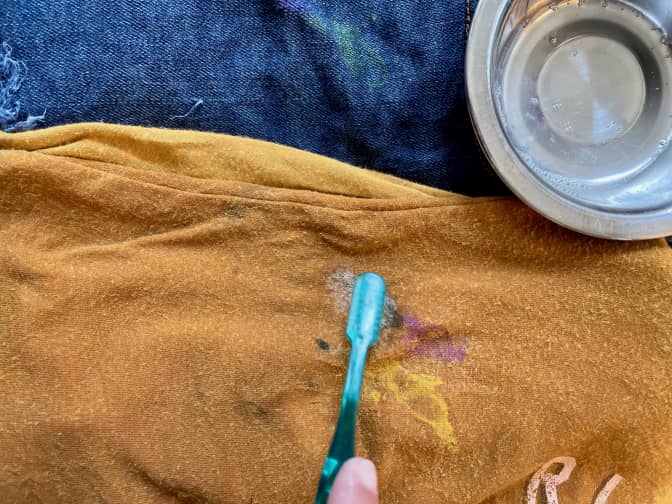 someone scrubbing paint out of a shirt with a toothbrush