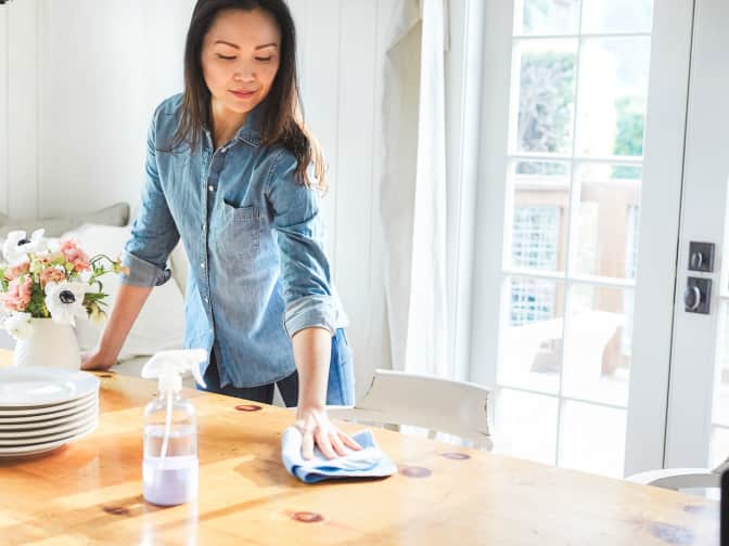 woman in chambray shirt wiping down wood table