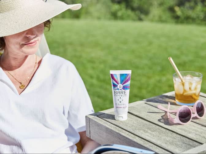 woman sitting outside in the backyard with a bare republic diamond dust sunscreen on the side table