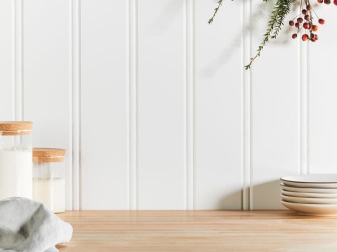 Image of white wood wall panels above wood counter with candles, plates, and plant