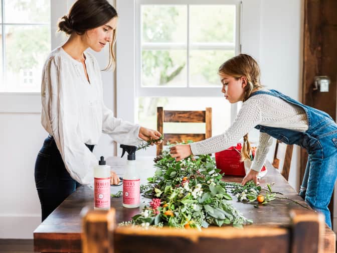Image of mother and daughter standing around wooden dining table looking at green centerpiece