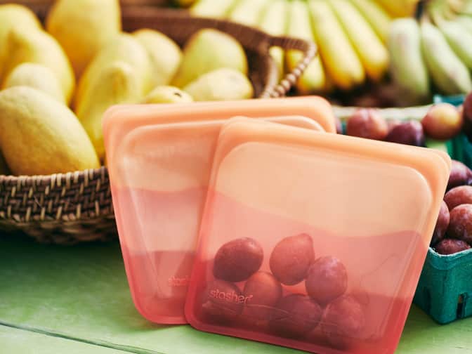 Image of grapes in a reusable storage bag with bananas and other fruit in background