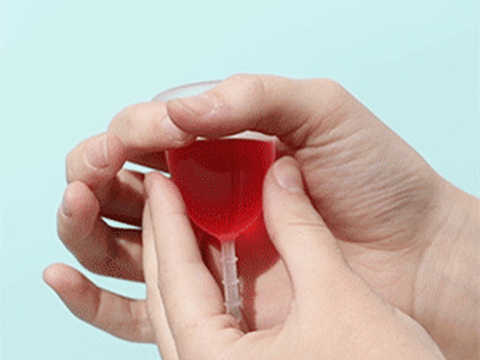Gif of someone holding a clear menstrual cup filled with red liquid squeezing it and pulling it out of hold made by thumb and forefinger