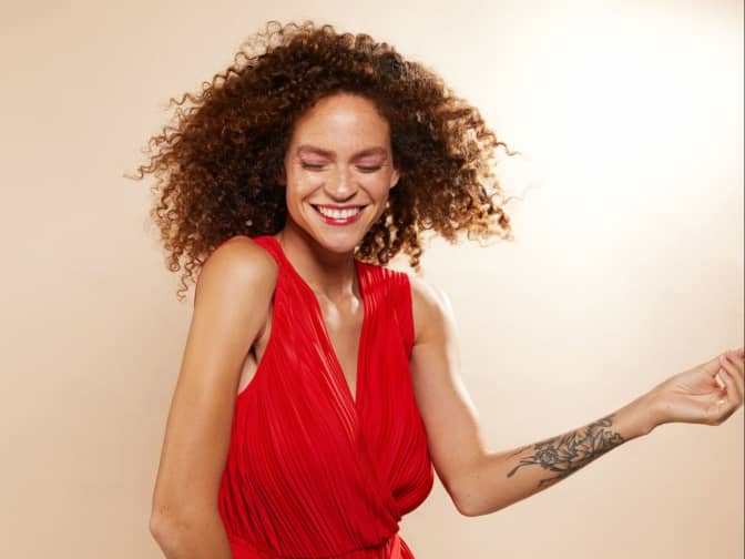 Curly haired woman in a red dress smiling in mid motion 