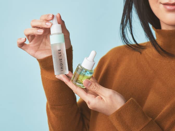 Photo of two skincare serums being held up by woman in orange turtleneck