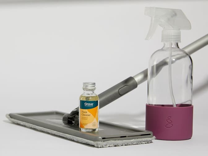 Image of Grove's Floor Cleaner concentrate on top a flat mop next to a glass spray bottle. 