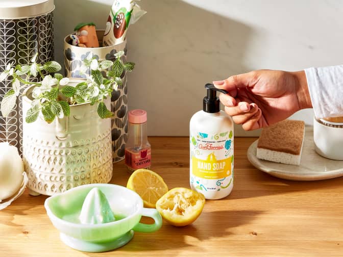 Image of person pumping Aunt Fannie's Hand Soap bottle sitting on wooden counter next to cut lemons and plants