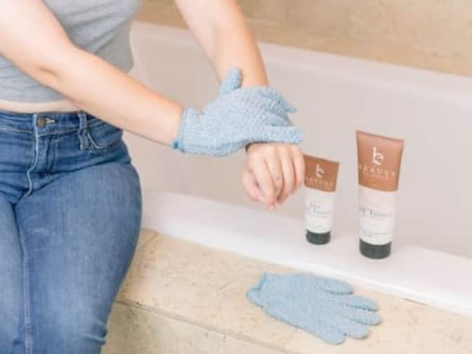 Image of person wearing exfoliating gloves wiping self tanner on arm