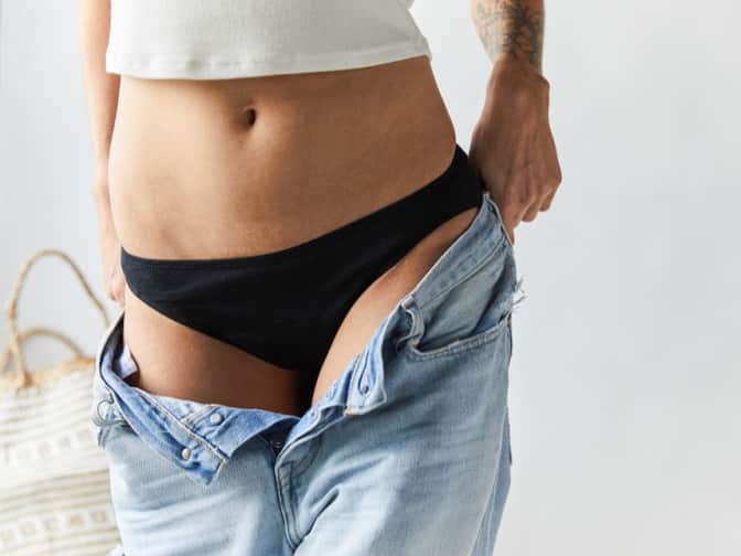 Image of a woman putting on jeans over period panties. 
