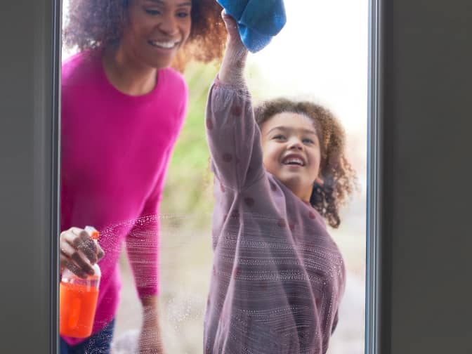 Image of mother and daughter cleaning class door with rag and orange spray bottle