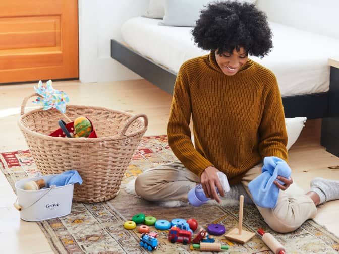 woman cleaning basket full of toys with spray bottle and cloth