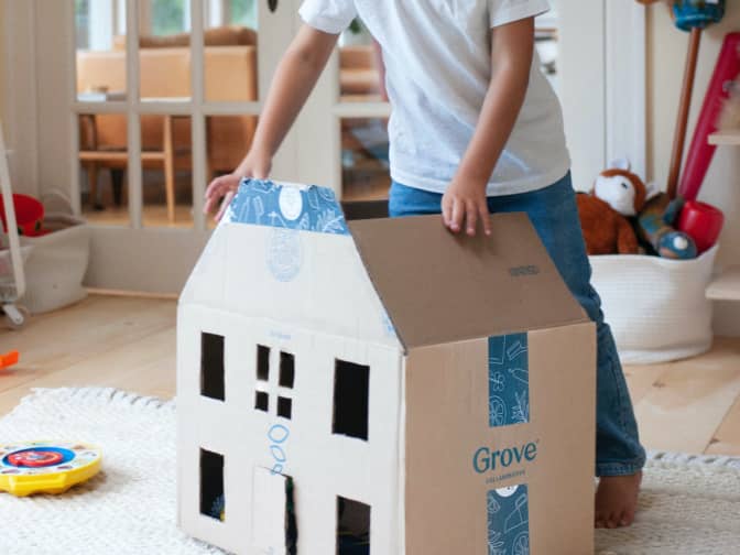 Image of Grove delivery box made into a kid's doll house for play with a kid standing above it