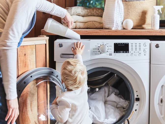Parent holding child's hand while they watch clothes spin in the dryer