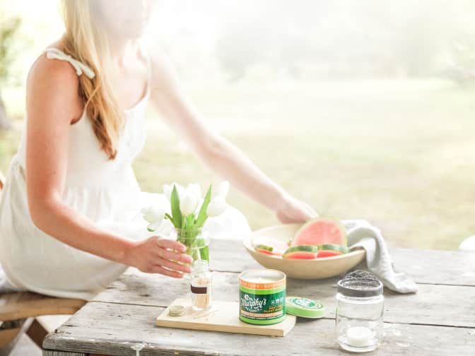 Young blonde woman placing a bowl of sliced watermelon onto a picnic table using Murphy’s Naturals mosquito candle