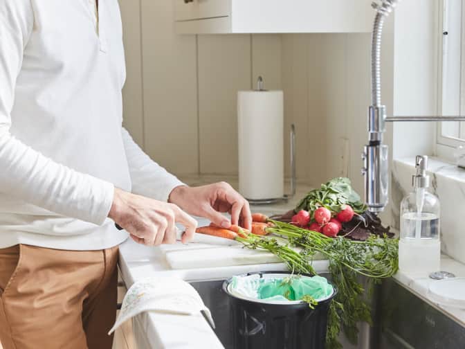 person chopping vegetables and compositing over the kitchen sink