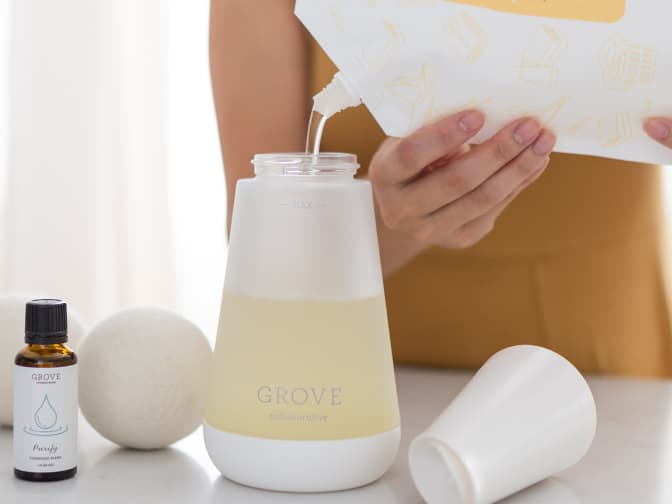 woman pouring detergent into into a grove laundry detergent dispenser bottle 