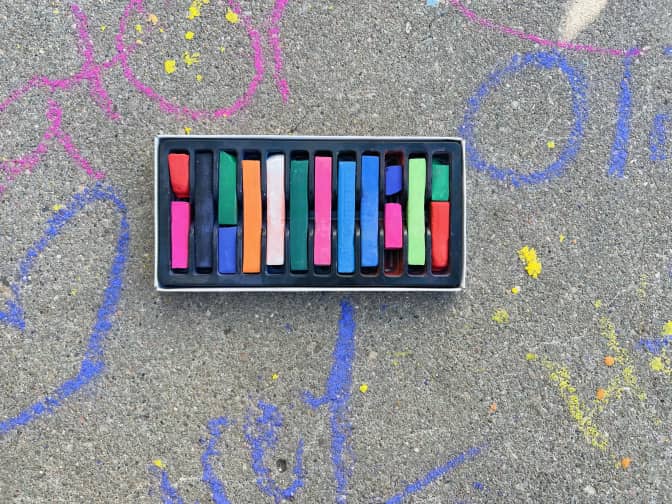 open box of Hair Coloring Chalk with chalk drawings on the cement