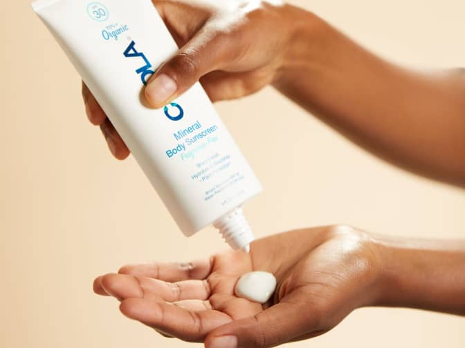 Person squeezing the COOLA mineral body sunscreen on to the palm of their hand