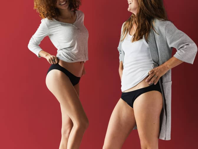 two women in tops and black period underwear against red background