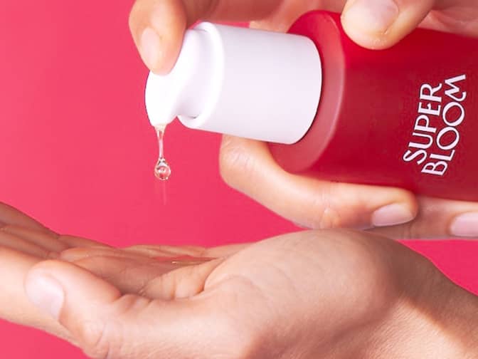 Photo of Superbloom cleansing oil pouring into hand against pink-red background