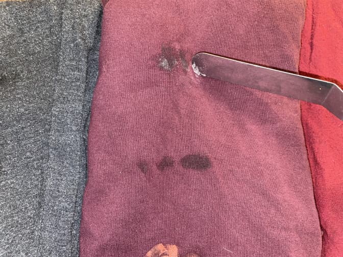 A shirt with chapstick being scraped by a thin metal spatula.