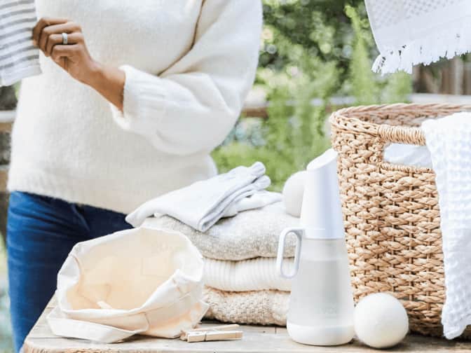 Image of woman folding clothes from laundry basket with Grove laundry vessel and one wool dryer ball out front on table