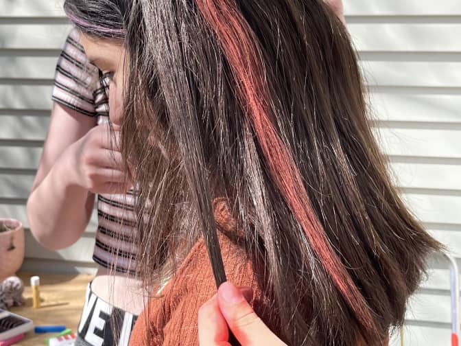 a vivid red streak from hair chalk in a child's long black hair