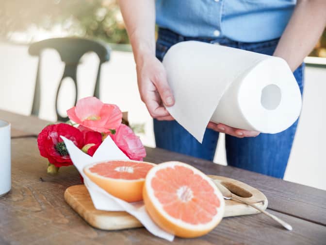 Woman about to pull a sheet from a paper towel roll she is holding in her hand to clean up from cutting a grapefruit