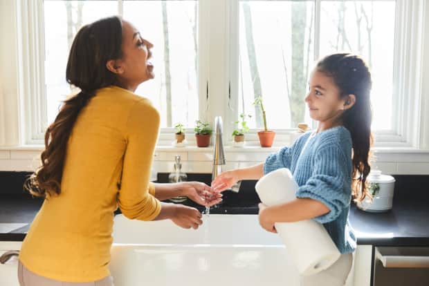 woman and child holding paper towel in front of sink with water running