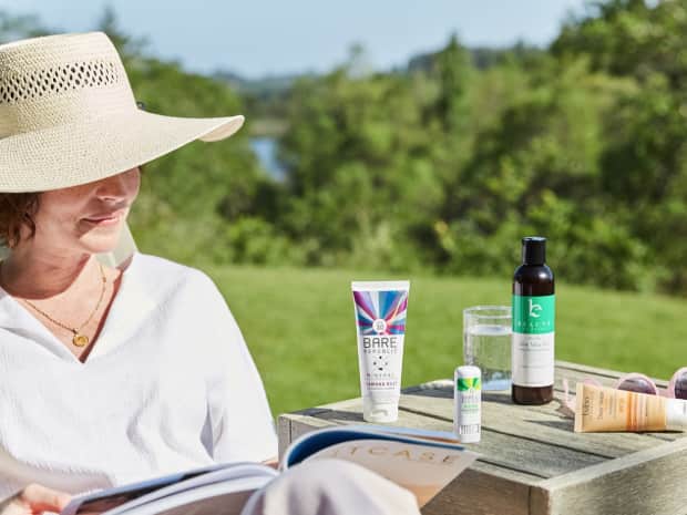 woman outdoors in a hat reading a magazine with sunscreen options on the table next to her
