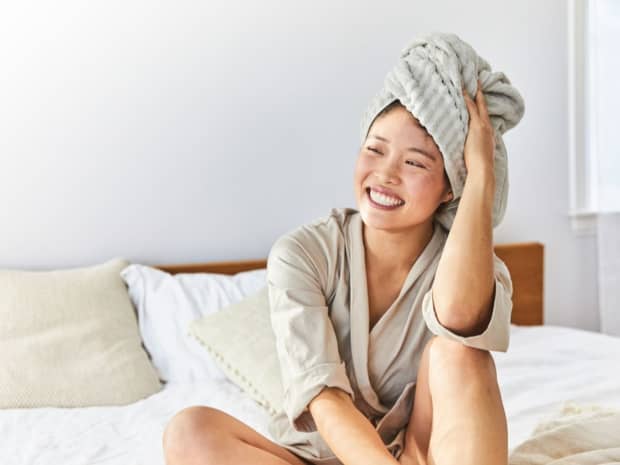 Image of a woman sitting in a bed with her hair wrapped in a towel.