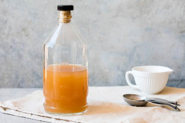 Photo of apple cider vinegar in bottle next to measuring spoons and cup