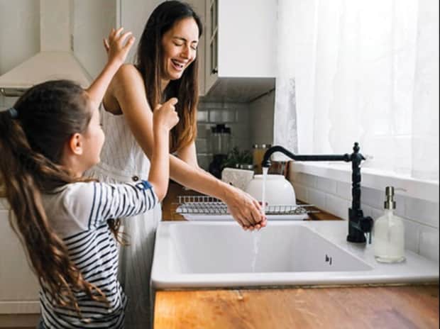 Woman and child washing hands in the kitchen sink and laughing