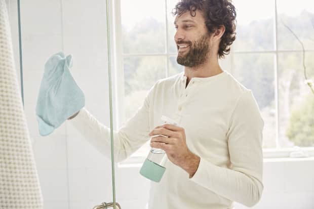 man cleaning shower with spray bottle and microfiber cloth