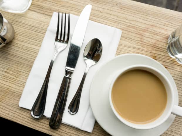 Image of a fork, knife, and spoon on top of a napkin next to a cup of coffee.
