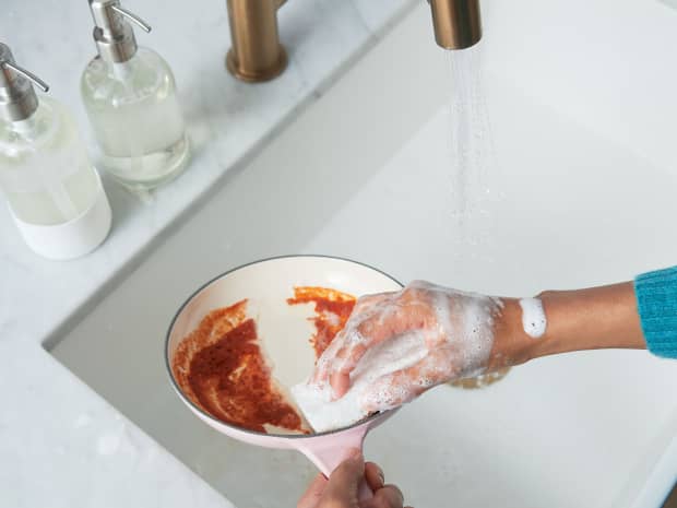Image of person with soapy hand holding sponge and washing dirty pan in kitchen sink