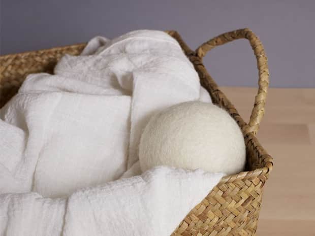 Image of white wool dryer ball in a basket of white linen laundry