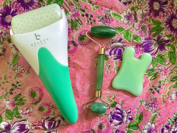 ice roller, jade roller and gua sha stone on a pink, floral background