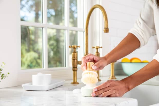 person using scrubber brush on brass sink