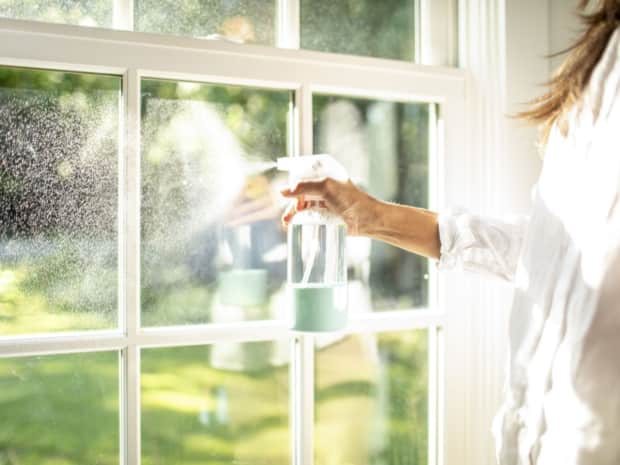 Image of a woman spraying a window with a reusable glass spray bottle 