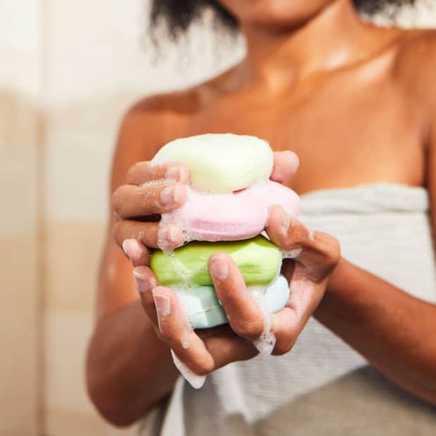 woman holding stack of bar soaps and shampoos