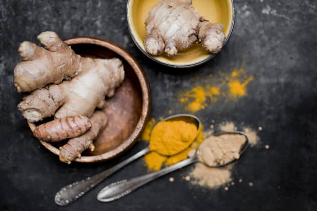 Turmeric and ginger roots in wooden bowls with powder in spoons