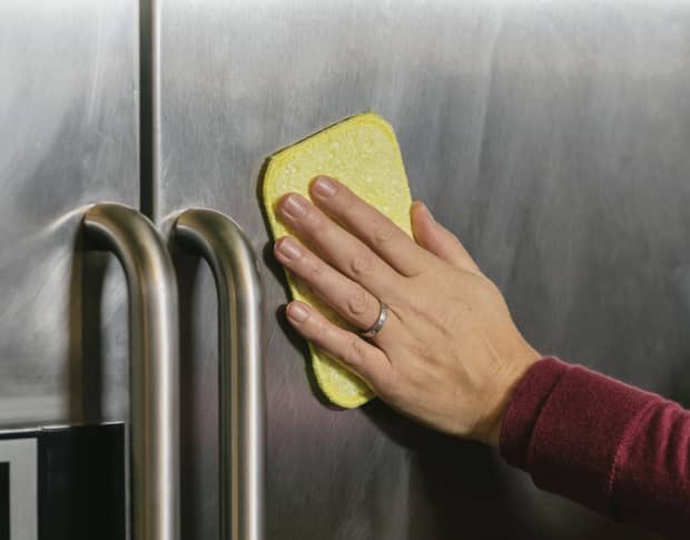 Image od someone wiping down a stainless steel fridge with a sponge.