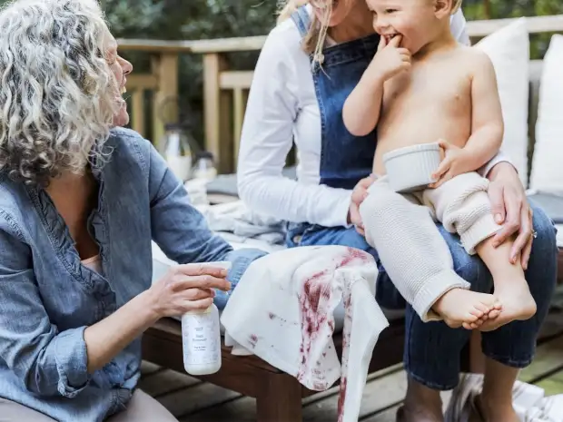 Image of a woman spraying a stain on laundry next to a woman holding a child. 