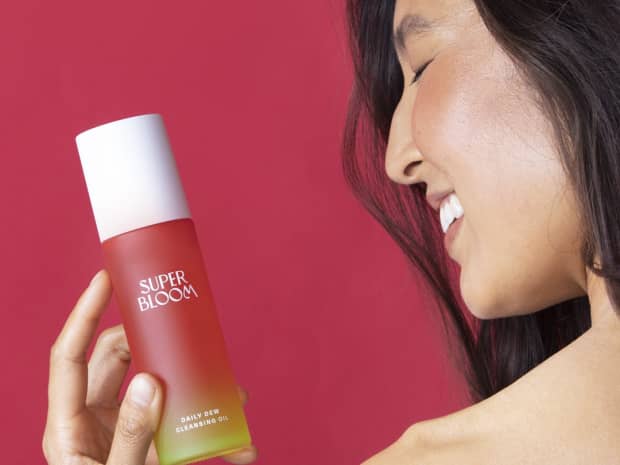 Photo of woman holding Superbloom Daily Dew Cleansing Oil against pink-red background