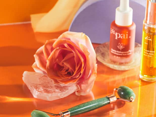 skincare products, rose, and jade roller arranged on a table